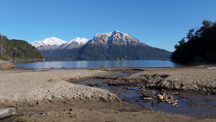Snowy Peaks Reflecting on Lake Nahuel Huapi, Patagonia, Argentina, with Serene Sandy Shoreline.