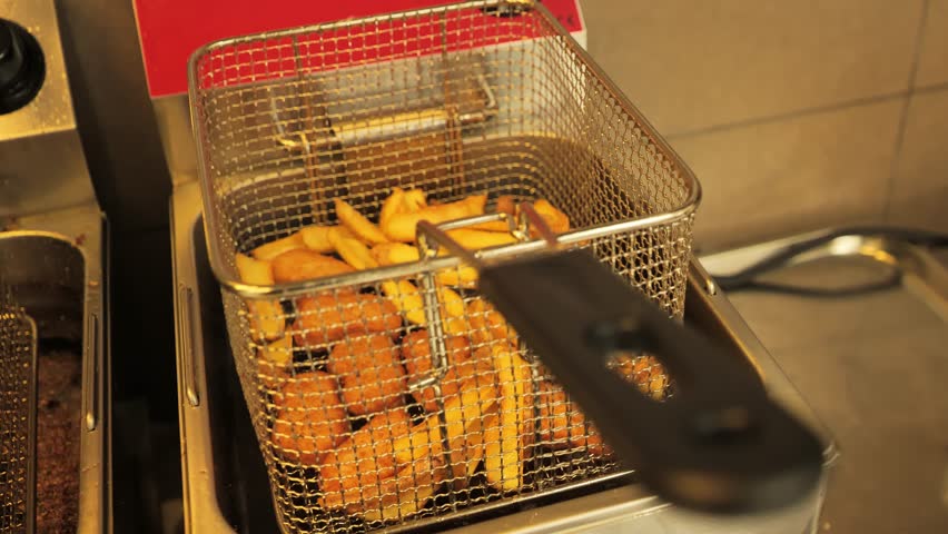 Frying basket with crispy fries and nuggets draining after deep frying in hot oil