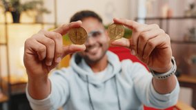 Indian man freelancer holding two gold coins, successful developer programmer. Guy stock trader earning bitcoins after online monitoring trading operations. Increasing wealth, financial prosperity - Powered by Shutterstock - Get 15% off with code: PIKWIZARD15