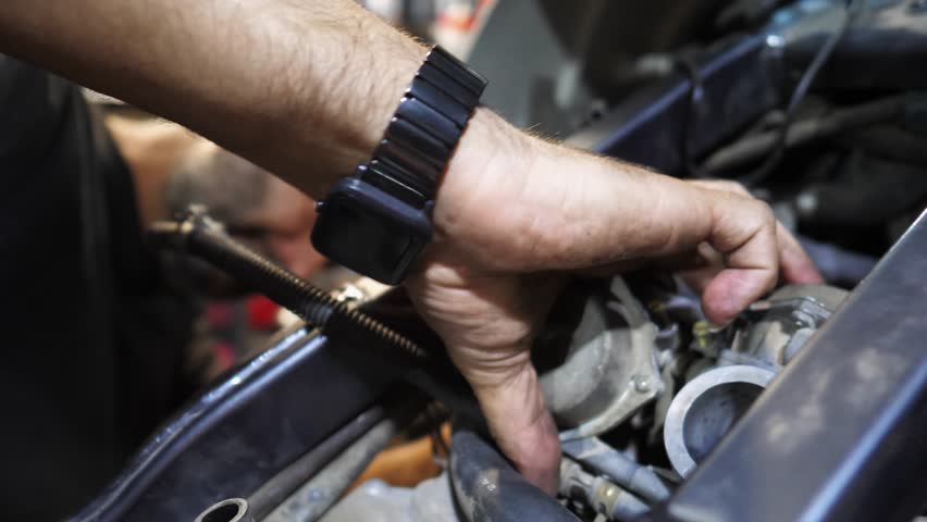 Male hands of repairer fixing moto engine at workshop. Arms of professional mechanic repairing detail of motorcycle at workplace. Adult repairman mending vehicle motor at garage. Maintenance service