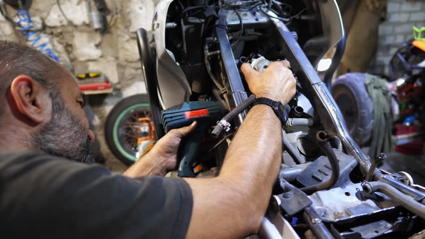 Professional mechanic repairing engine of motorcycle at workshop. Male repairer fixing motor of motorbike using tool at workplace. Adult repairman working at garage. Concept of maintenance service - Powered by Shutterstock - Get 15% off with code: PIKWIZARD15