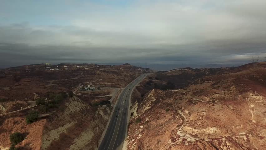 Aerial view of traffic on highway between desert mountains of California, USA. Cloudy day in USA. Wide shot.