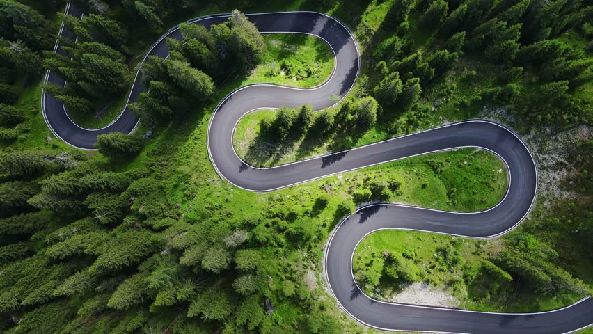 Passo Giau’s iconic curves, captured from above, surrounded by lush forests, Iatly