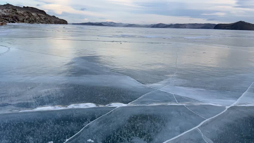 Video of Baikal Lake in December. Panoramic view of blue clear ice with cracks of frozen Kurkut Bay of Small Sea Strait at sunset. Beautiful winter landscape. Nature background