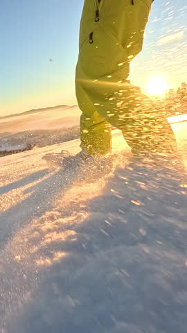SLOW MOTION, LOW ANGLE, CLOSE UP, LENS FLARE: Unrecognizable male snowboarder rides fresh powder on a sunny December evening as his pet dog runs ahead. Cool shot of snowboarding with dog at sunset.