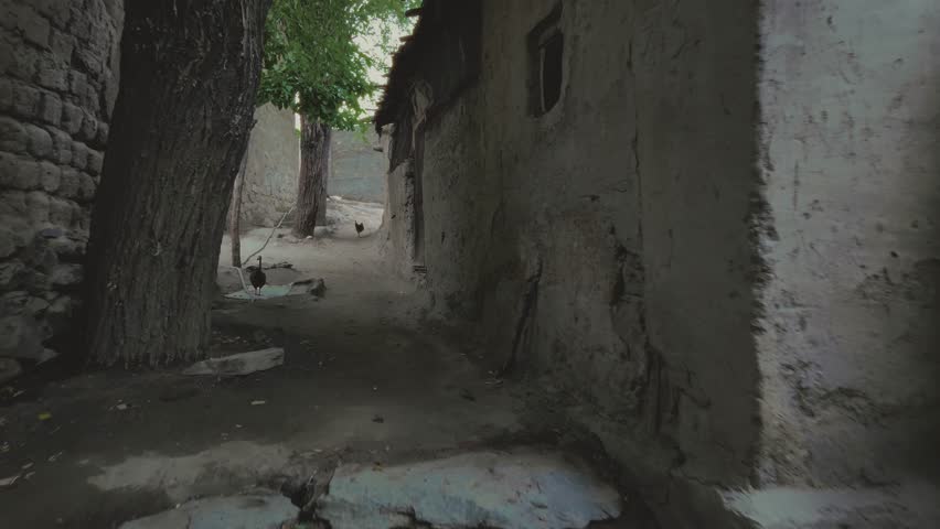 A footage of a narrow street between old, rustic buildings, with hens walking around in a village in Skardu, Pakistan