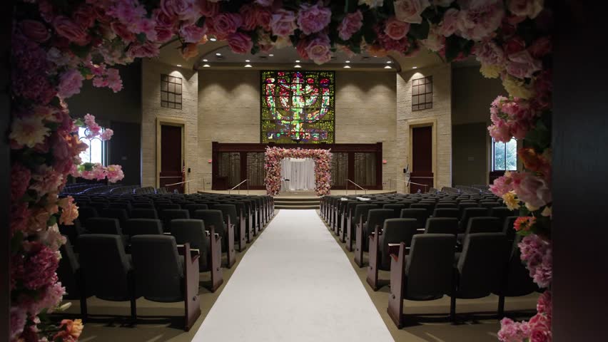 Wide-angle view of a beautifully decorated chapel for a wedding ceremony. Features floral arch, stained glass windows, and modern seating. Ideal for event planning or venue promotions.
