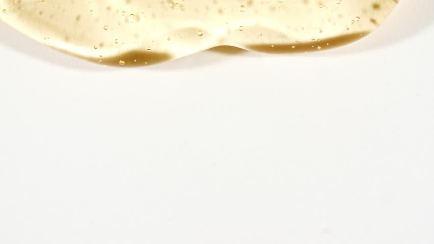 Yellow Transparent Cosmetic Gel Fluid With Molecule Bubbles Flowing On The White Surface. Macro Shot. Liquid Cream Gel Transparent Cosmetic Sample Texture With Bubbles.