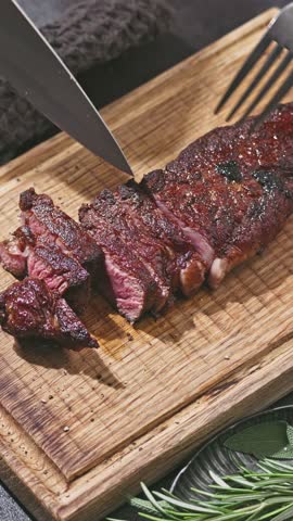 Chef slicing freshly grilled juicy wagyu beef steak meat with a knife on a wooden cutting board in the kitchen, food close-up