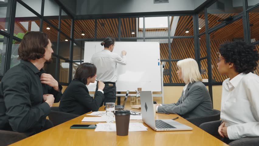 Diverse co-workers in office, creative designers discussing and making decisions. Team of multinational professionals looking at laptop display, talking about business idea and sales reports, teamwork