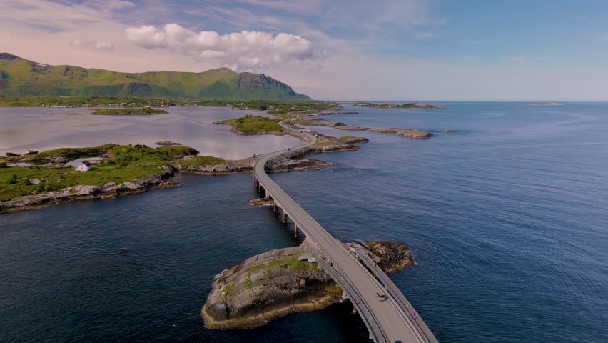 Witness the beauty of Norways coastline as vehicles traverse a magnificent road surrounded by serene waters and lush green hills. Atlantic Ocean Road (Atlanterhavsveien) in Norway