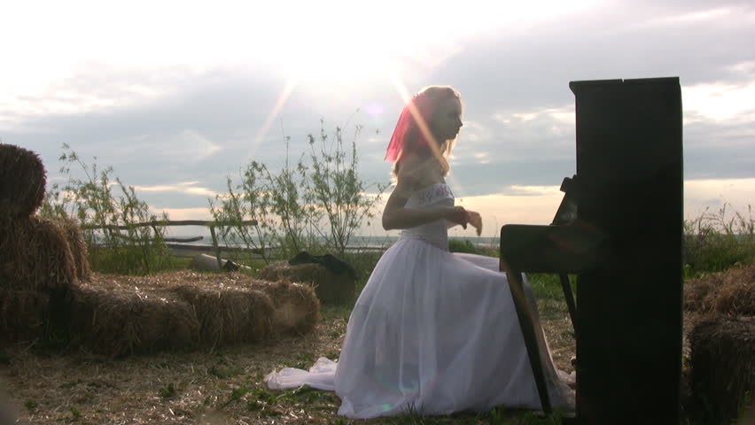 Bride in wedding dress plays the piano, which stands in the steppe on the