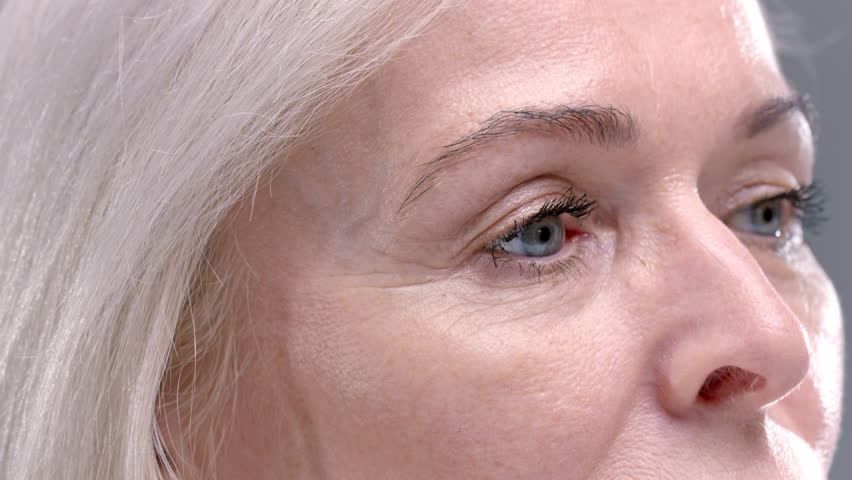 Close up: old woman paints her eyelashes with mascara. Senior female puts mascara on her eyes, expressive blonde look. Carefree pensioner portrait, good eyesight after vision correction. Elderly lady