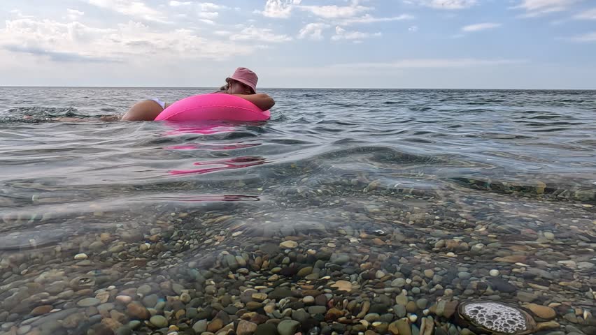 Woman Beach Floating - A woman in a pink swimsuit floats in the water at a beach on a sunny day.