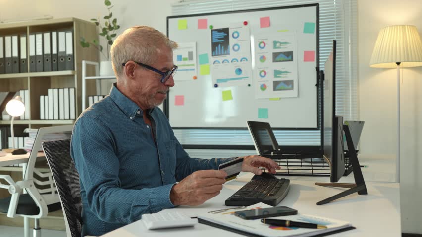 Happy businessman using credit card for online shopping on computer in modern office, enjoying purchasing goods or services remotely, feeling satisfied with secure and convenient payment method
