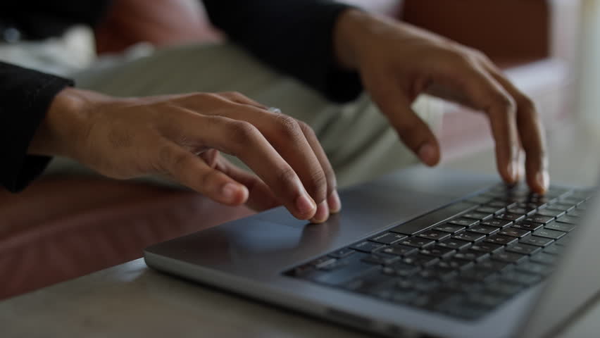 Close-up of hands browsing online on a laptop keyboard in a modern workspace