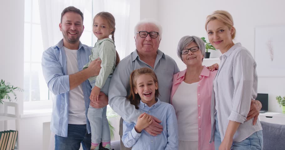 Portrait of joyful smiling big family of parents, grandparents and children standing in the living room at home and looking cheerful at camera. Happy family concept. 4k video. Slow motion video.