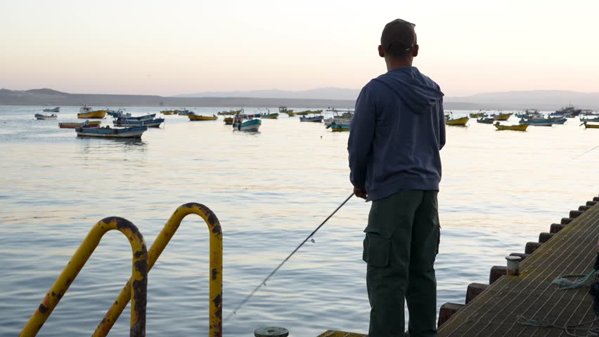 Fisherman casting line from pier with colorful boats in background in Tongoy, Coquimbo region