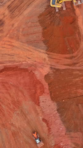 Excavating equipment operates loads red earth to dump truck at construction site during construction building home reshaping the landscape.