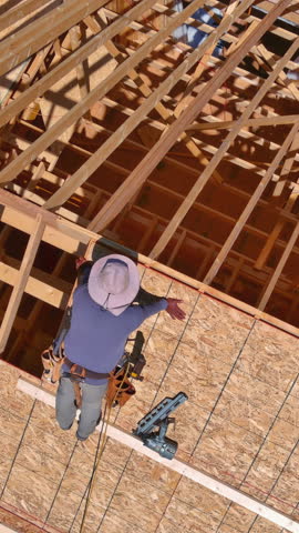 Construction worker is applying roof sheathing wooden plywood top wooden framework at building site during construction home