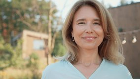 Front view of gorgeous Caucasian woman with blond hair standing outside. Turning her head and looking at camera while smiling. Enjoying warm sunny weather. Wearing earrings and blue shirt. - Powered by Shutterstock - Get 15% off with code: PIKWIZARD15