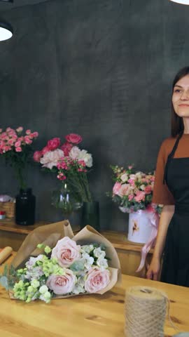 A young woman florist in a flower shop gives a bouquet to the customer. Buyer of a bouquet. Retail sale of flowers. Small business, flower shop owner hands over bouquet to customer.