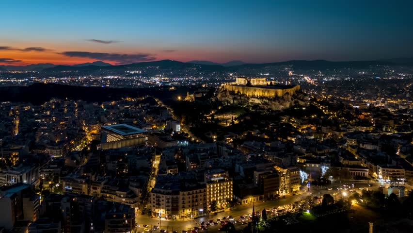 Aerial hyperlapse view of the city center of Athens, Greece, with the illuminated Parthenon Temple at the Acropolis at dusk