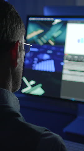 A man is focused on detailed data analysis on his computer in a dimly lit environment