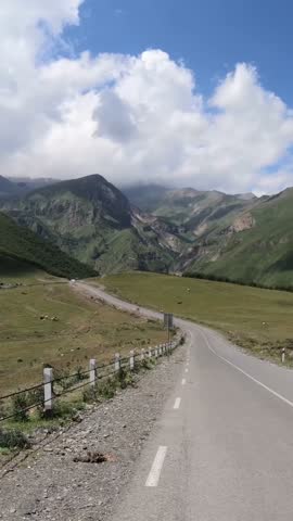 Vertical. Driving on the road in a mountain alley with a view of the mountain ranges and the sky