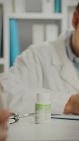 A healthcare professional in a white coat explains medication options to a patient at a desk. The interaction takes place in a well-organized clinical environment with medication containers visible