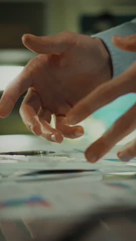 Two hands reach out to discuss and organize various documents and materials on a table in a bright workspace. The atmosphere is collaborative and focused on teamwork