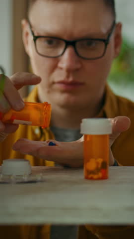 A man focuses intently as he pours pills from a prescription bottle into his hand. The well-lit space emphasizes his concentration on managing his medication