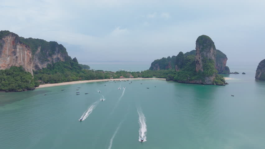 Experience the beauty of Krabi, Thailand, with stunning aerial views of traditional longtail boats gliding over turquoise waters, surrounded by majestic limestone cliffs