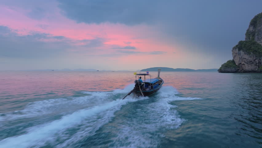 An aerial view captures a longtail boat gliding through Krabis tranquil waters at sunset, showcasing vibrant colors and serene landscapes that epitomize natural beauty