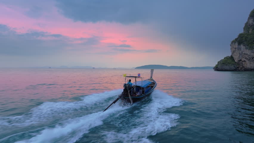 An aerial view captures a longtail boat gliding through Krabis tranquil waters at sunset, showcasing vibrant colors and serene landscapes that epitomize natural beauty