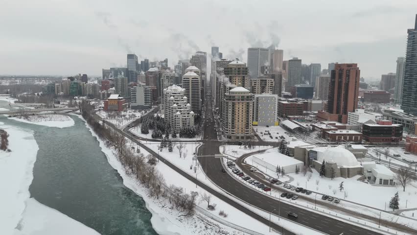 Aerial tracking shot snow covered city with heat vapours rising from tower blocks and apartment buildings during winter.