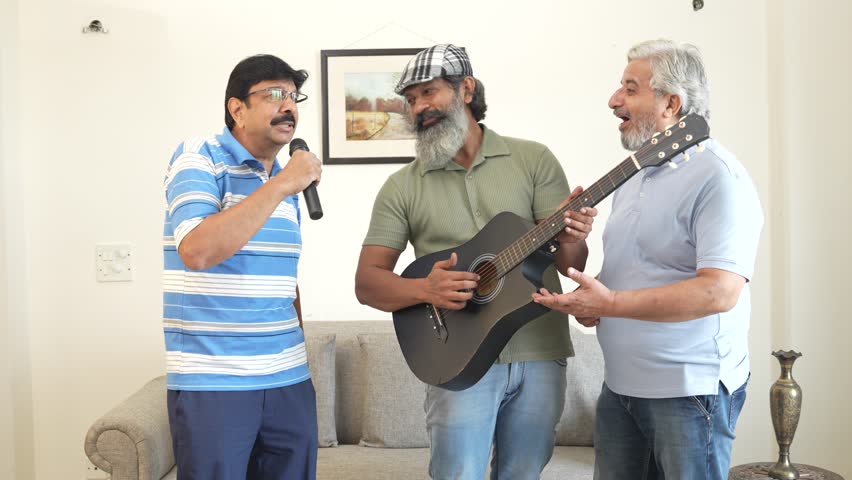 Group of senior indian friend playing guitar, singing and enjoy dancing in living room at home. Mature elderly men having party celebrate weekend reunion gathered together in house, Retirement life. 