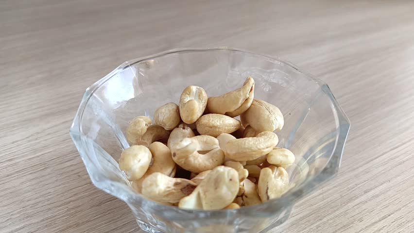 Cashew nuts are poured into a cup on the table. High protein content in nuts. Fresh peeled cashews.