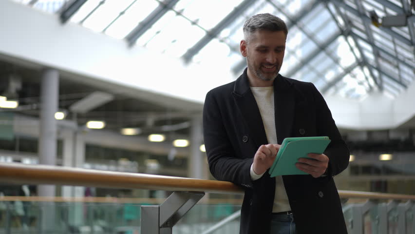 A fashionable man is interacting with a sleek tablet while situated in a modern and stylish indoor setting