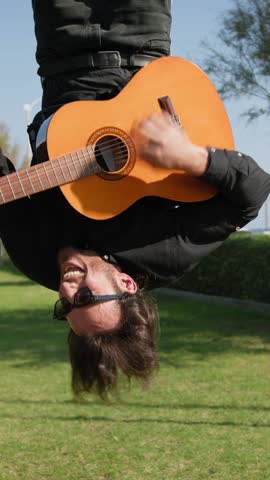 Young Man Plays Guitar Music Hanging Upside Down In An Outdoor Park