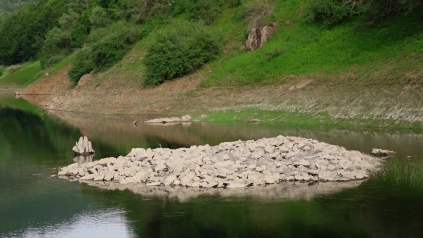 Low water levels reveal rocky island in mountain lake during summer season