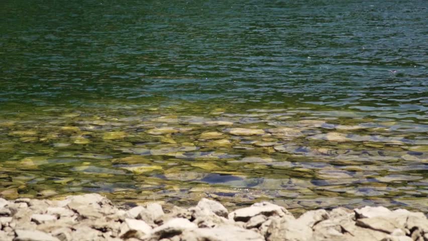 Calm water reflections with stones along the shore at a serene lake in the afternoon sun
