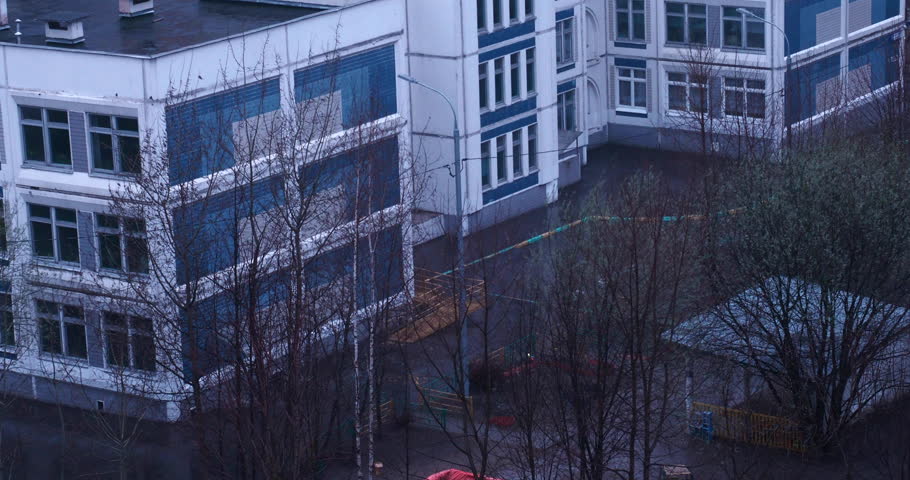 A kindergarten yard drenched in heavy autumn rain, featuring wet asphalt and bare trees, evokes a poignant sense of nostalgia and sadness.