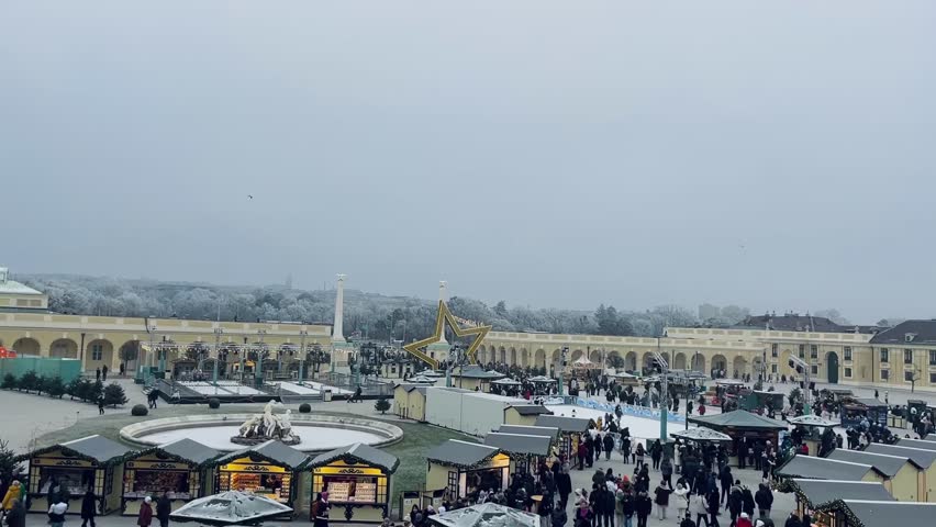 View from above of the festive traditional Schönbrunn Christmas Market Weihnachtsmarkt full of tourists and locals buying souvenirs during a cold winter snowy day, Christmas Eve, in Vienna, Austria