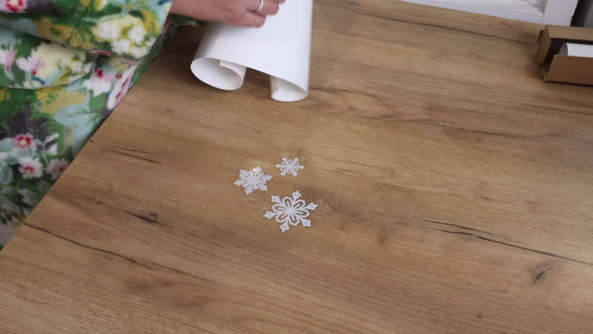 A woman removes snowflake stickers from a paper backing and places them on the table. Vertical video.