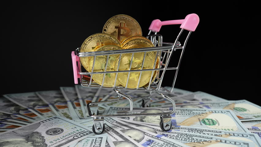 Shopping cart on wheels with gold bitcoin coins in it on american hundred dollar bills, close up, rotates. Finance, business, digital money and bitcoin concept