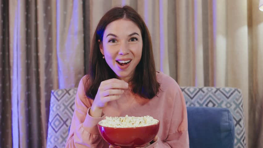 An Excited Woman Enjoying a Movie with Popcorn in Her Cozy Living Room, Surrounded by Comfort and a Relaxing Atmosphere for Entertainment