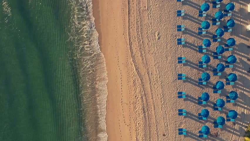 A perfect overhead view of umbrellas and chairs on a Florida beach early in the morning with Clearwater and waves and people walking on vacation cinematic epic symmetrical vacation travel tourism