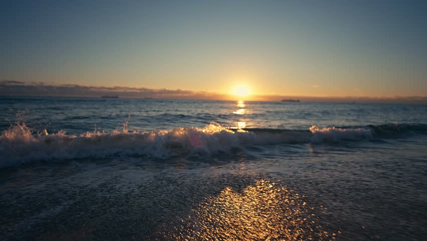 The sun is rising over a perfect beach with small waves in Florida with reflective colors and a cinematic shallow of the field on a perfect morning colorful beautiful sunset