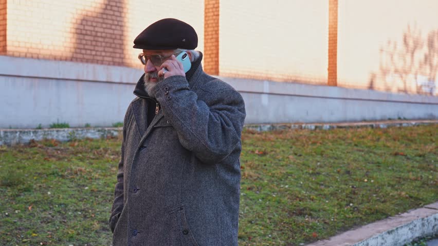 Elder grey haired man in the morning outside, man enjoying his morning walk in the city, walking on the street talking on smartphone. Daily routine lifestyle concept.